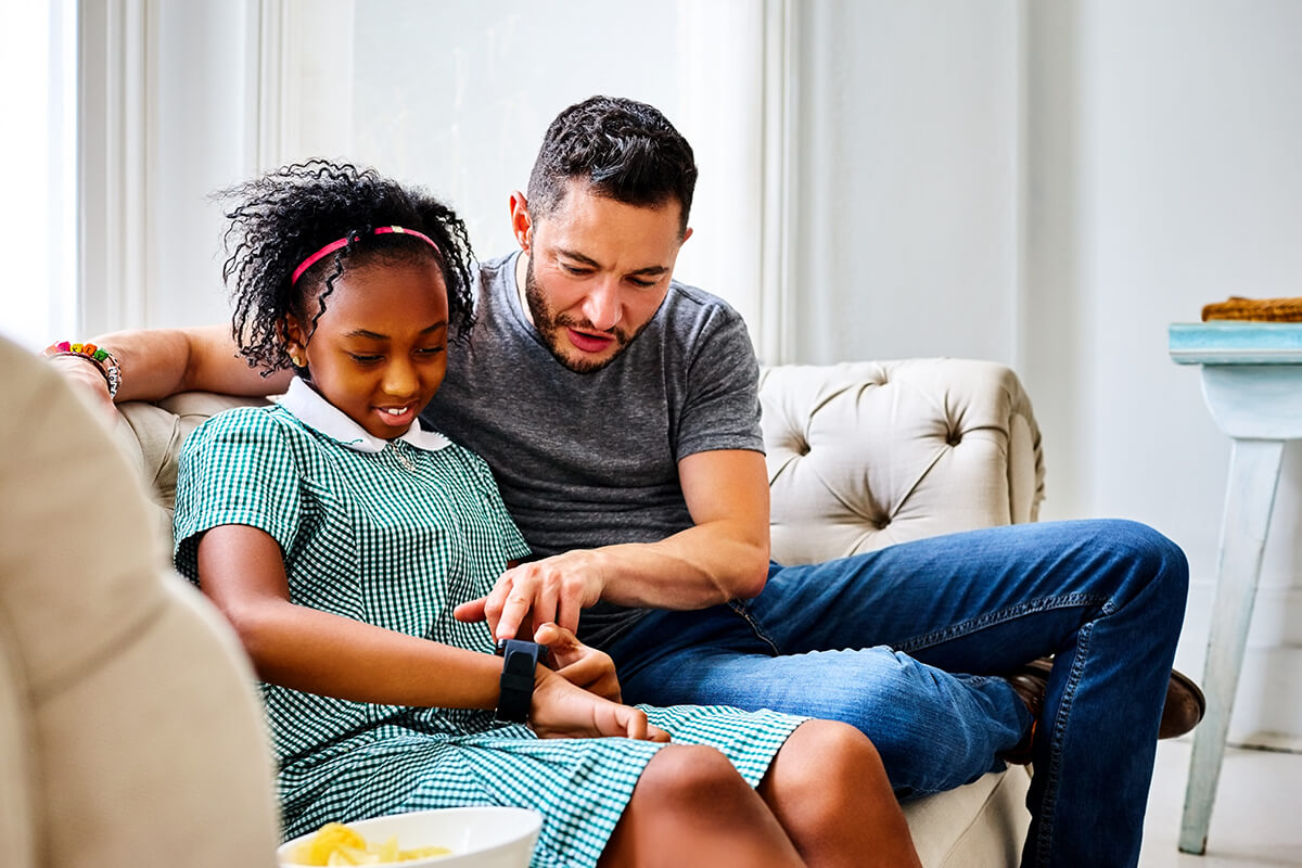 Transgender father with daughter using smart watch at home