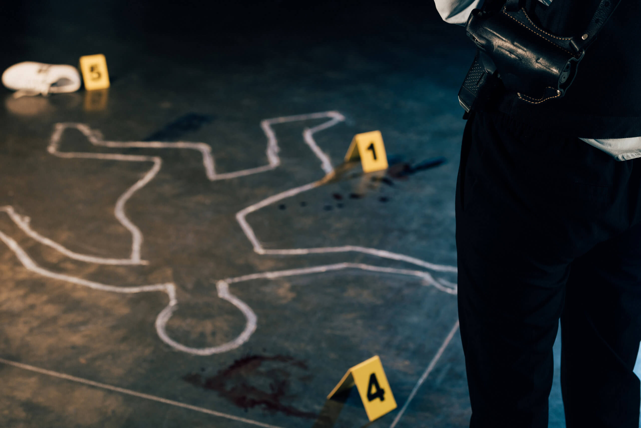 cropped view of investigator standing near chalk outline and evidence markers at crime scene